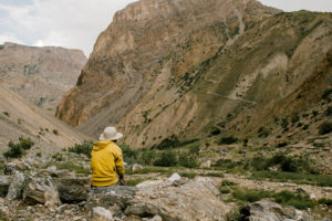 Anonymous hiker enjoying mountain view sitting on stone in valley