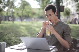 Black man drinking lemonade in cafe and using laptop