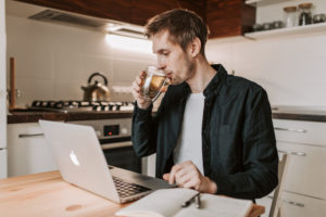 Businessman drinking cup of tea while watching laptop in kitchen at home
