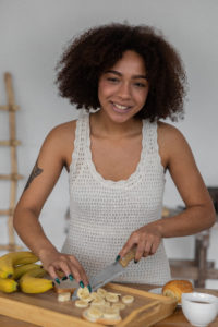 Cheerful black woman cutting banana for breakfast