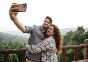 Cheerful young couple hugging while taking selfie on terrace in forest