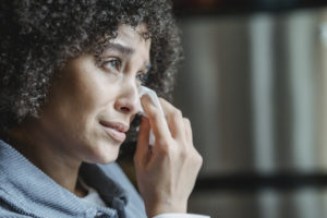 Crying ethnic female wiping tears with napkin