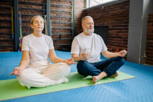 Elderly people sitting on yoga mat while meditating