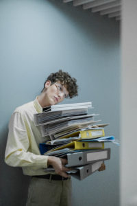 Person in yellow long sleeve shirt carrying stack of office files