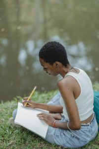 Serious black student writing essay in notebook in park