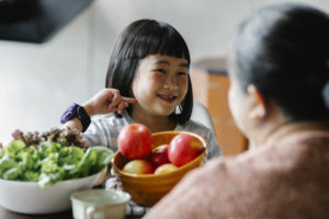 Smiling funny asian girl smiling while having breakfast with mother