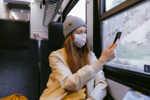 Woman in beige jacket and gray knit cap holding smartphone