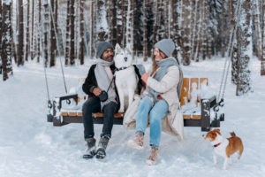 Woman in white jacket sitting on brown wooden bench beside white and brown dog on snow