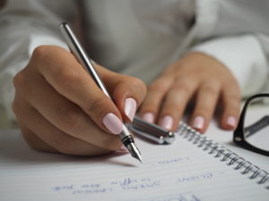 Woman in white long sleeved shirt holding a pen writing on a paper