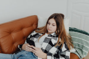Teenage girl lying on the sofa and looking at her smart phone