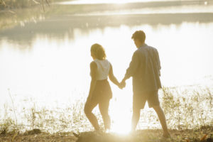 Unrecognizable couple holding hands during stroll on lake coast