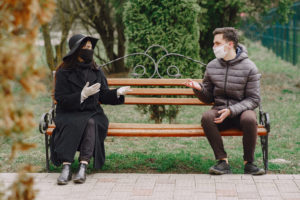 Young couple in protective gloves and masks chatting on bench in park